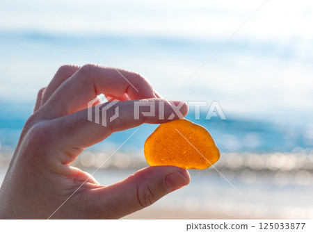 Hand holding amber stone against sunny seaside background 125033877