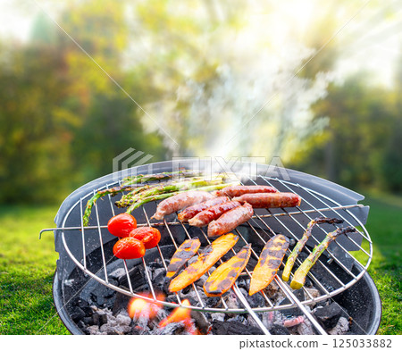 close-up top view of a charcoal grill with sausages, asparagus and cherry tomatoes being grilled outdoors at backyard close-up top view of a charcoal grill with sausages, asparagus and cherry tomatoes being grilled outdoors at backyard 125033882