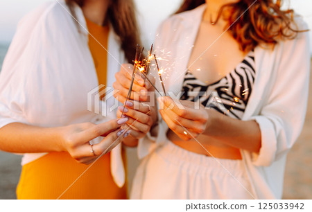 Beautiful Two women holding sparkler celebration on beach. They are having a great time together! Beautiful Two women holding sparkler celebration on beach. They are having a great time together! 125033942