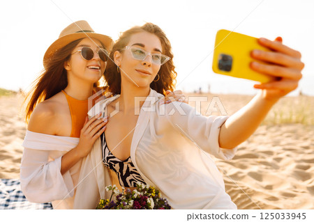 Two pretty friends women making selfie on beach, light and bright summer colors. Friends together 125033945