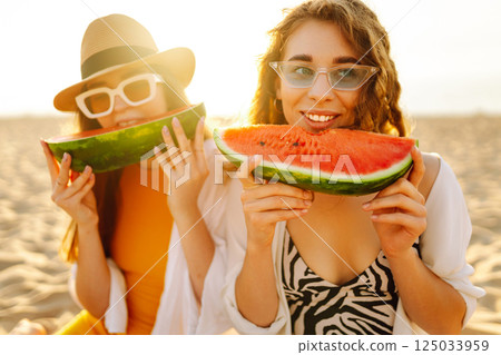 Smiling two women eating watermelon on beach. Happy summer time. People, lifestyle, travel 125033959