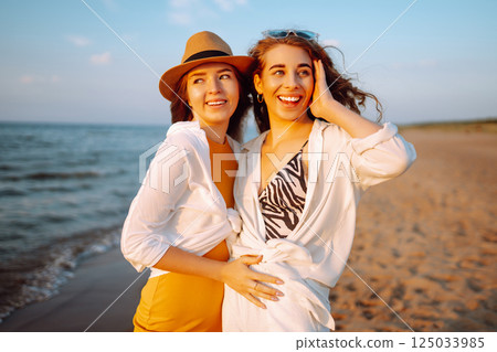 Portrait of two young female friends walking on the sea shore at sunset. Lifestyle concept. 125033985