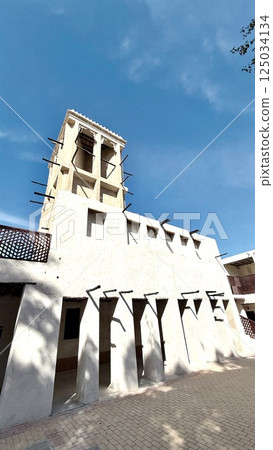 Arabic fort architecture surrounds garden walkway as bright sun highlights Arabic fort textures, evoking historic beauty through sandstone tones and peaceful cultural atmosphere. 125034134