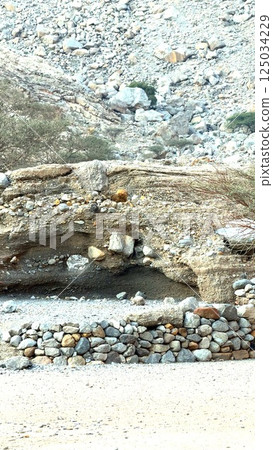Sunlit village with natural caves hidden in rugged hills. Stone walls and carved dwellings reflect historical legacy. Remote landscape highlights cultural heritage of settlement. Sunlit village with natural caves hidden in rugged hills. Stone walls and carved dwellings reflect historical legacy. Remote landscape highlights cultural heritage of settlement. 125034229