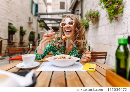 Young woman sitting in summer cafe, eating pasta with tomato, meat. Bolognese. Parmesan cheese. 125034472