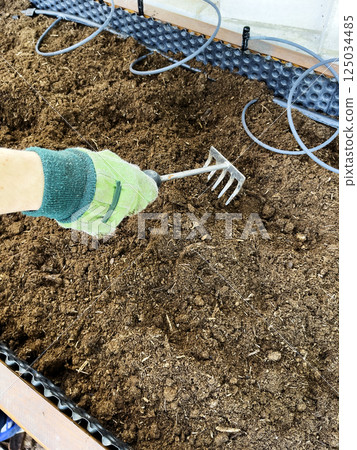 Men's hand in green gloves prepare the soil for planting in spring. The soil is distributed with a rake. 125034485