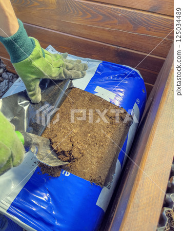 Men's hands in gloves prepare soil for planting in spring. Cutting the soil package with pruning shears. 125034489