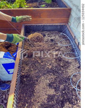 Men's hands in gloves prepare soil for planting in spring. Distributing the soil with a trowel. 125034492