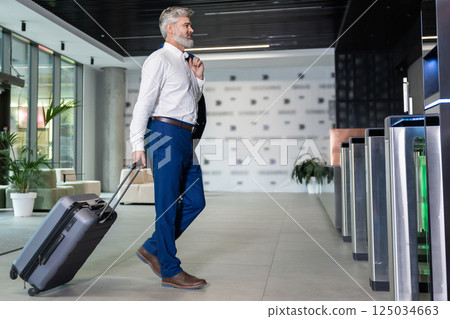 Bearded man walking in airport terminal carrying suitcase 125034663