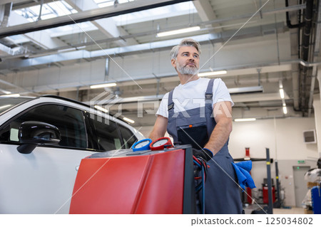 Bearded man technician checking car air conditioning system refrigerant recharge Bearded man technician checking car air conditioning system refrigerant recharge 125034802