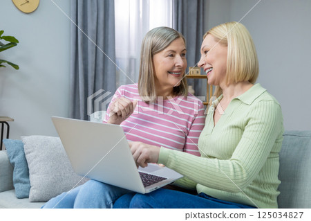 Two women looking old photos on laptop and looking happy and contented Two women looking old photos on laptop and looking happy and contented 125034827