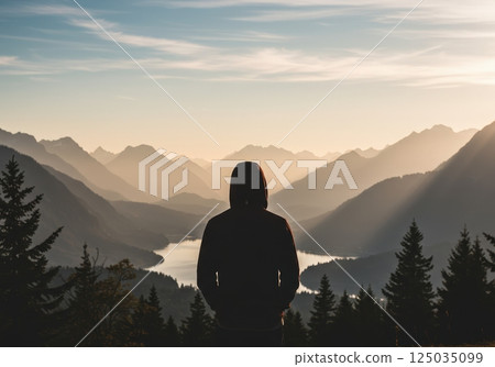Person overlooking a mountain landscape at sunset with lake and trees in view Person overlooking a mountain landscape at sunset with lake and trees in view 125035099