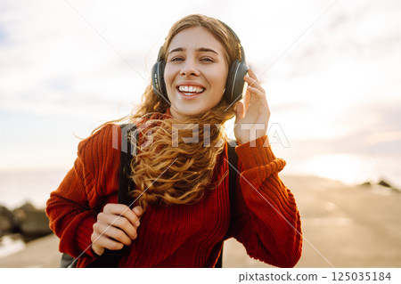 Happy woman listening nice music by the waterfront while wearing headphones by a lighthouse. 125035184