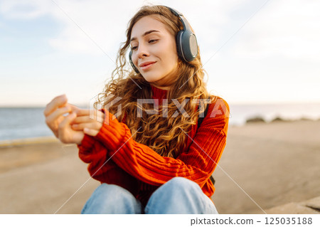 Happy woman listening nice music by the waterfront while wearing headphones by a lighthouse. Happy woman listening nice music by the waterfront while wearing headphones by a lighthouse. 125035188