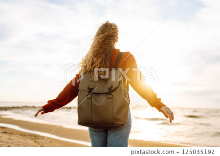 As she walked along the beach, the woman tourist adjusted her backpack, taking in the salty sea air As she walked along the beach, the woman tourist adjusted her backpack, taking in the salty sea air 125035192