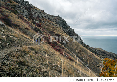 Hikers navigate rocky terrain along a coastal path under overcast skies in a remote landscape 125035767