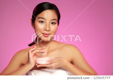 Model showcasing skincare product with pink background at studio setting during day 125035777