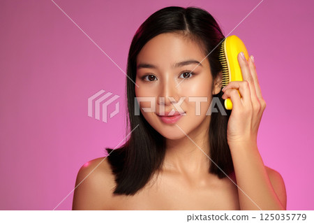 Woman with short hair holds yellow comb against her face in a vibrant pink background during a studio photoshoot Woman with short hair holds yellow comb against her face in a vibrant pink background during a studio photoshoot 125035779