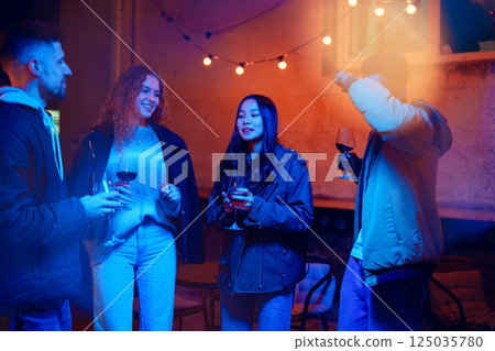 Friends celebrating together at night with drinks and laughter in a vibrant outdoor setting Friends celebrating together at night with drinks and laughter in a vibrant outdoor setting 125035780