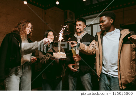 Friends celebrate birthday with cake and sparklers in cozy indoor setting Friends celebrate birthday with cake and sparklers in cozy indoor setting 125035800