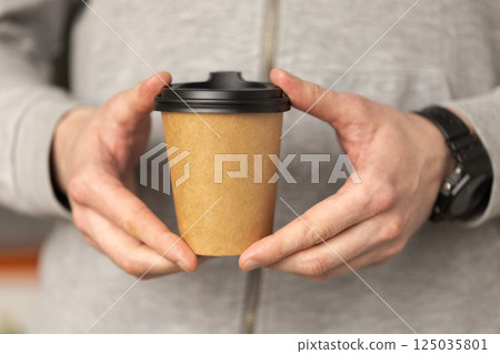 Man's hands holding a craft disposable paper cup with fresh coffee. 125035801