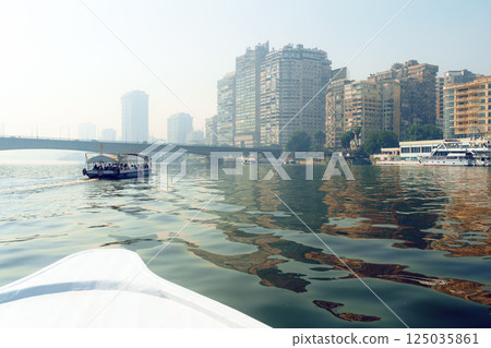 Beautiful skyline of Cairo reflected in the Nile with boats cruising along the calm waters in the early morning mist 125035861