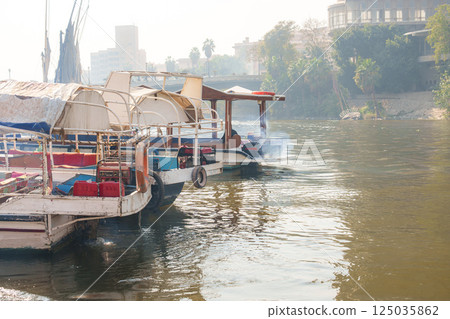 Boats navigate the river as mist envelops the banks in a tranquil morning setting 125035862