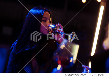 Woman enjoying a drink in a trendy venue during a nighttime social gathering with vibrant lighting Woman enjoying a drink in a trendy venue during a nighttime social gathering with vibrant lighting 125035910