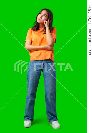 Young woman in casual attire deep in thought against a bright green background during a creative brainstorming session 125035952