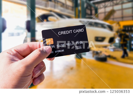 Paying for Car Repair , A hand holds a black credit card in a car repair shop 125036353