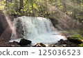 A landscape photo of a waterfall with rays of light shining through it in the forest 125036523