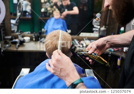 Hairdresser using electric shaver to cut boy's hair. Little kid getting first haircut in barbershop. Close up Hairdresser using electric shaver to cut boy's hair. Little kid getting first haircut in barbershop. Close up 125037074