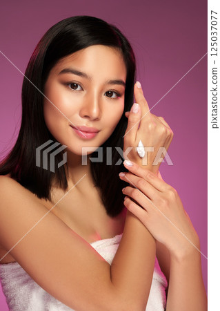 Young woman applying skincare product on hand with soft lighting and purple background during indoor photoshoot Young woman applying skincare product on hand with soft lighting and purple background during indoor photoshoot 125037077