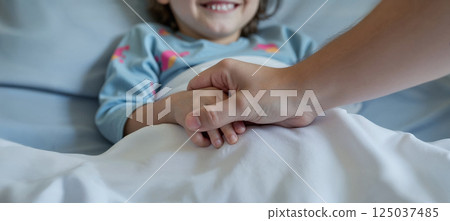 Touching hospital scene with a kid. The adult is holding her hand with care. Focus on hands 125037485