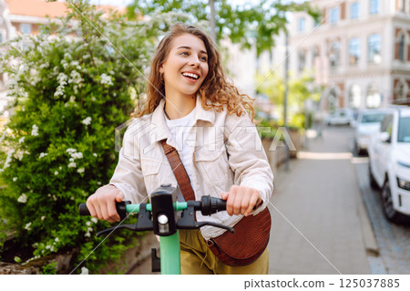 Happy woman rides an electric scooter in the city street on a sunny day. Ecological transport. 125037885