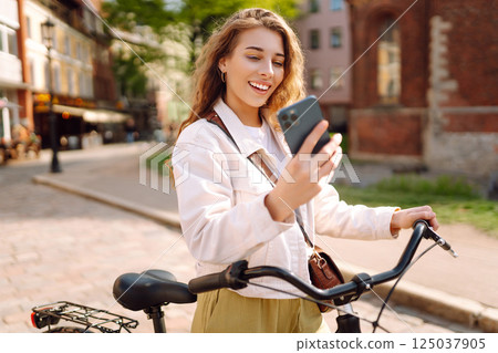 Young woman using mobile phone while riding bicycle at the city street outdoor. Selfie time. 125037905