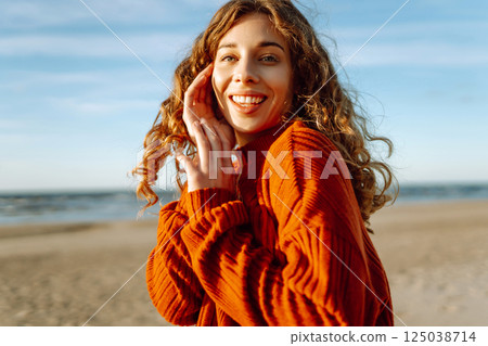 Portrait of curly woman on beach in cold sunny weather. Travel, weekend, relax and lifestyle concept Portrait of curly woman on beach in cold sunny weather. Travel, weekend, relax and lifestyle concept 125038714
