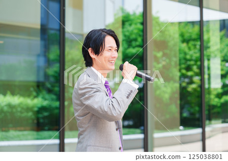 A man in a suit giving a speech on the street using a microphone 125038801