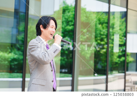 A man in a suit giving a speech on the street using a microphone 125038803