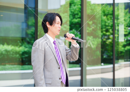 A man in a suit giving a speech on the street using a microphone 125038805