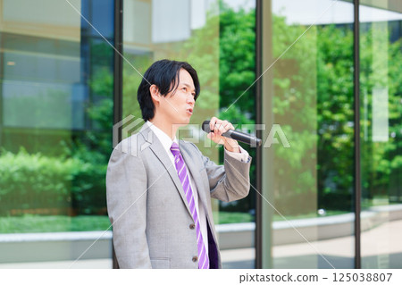 A man in a suit giving a speech on the street using a microphone A man in a suit giving a speech on the street using a microphone 125038807