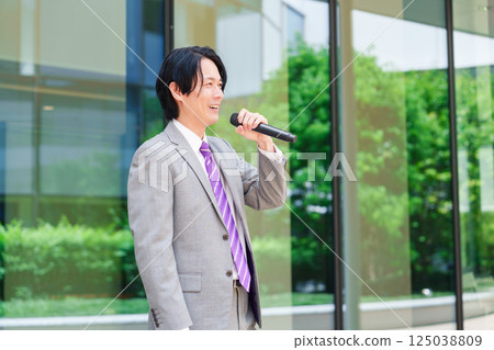 A man in a suit giving a speech on the street using a microphone 125038809