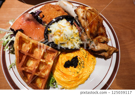 close up of an English full all day breakfast with truffle scrambled eggs, waffle, smoke salmon, mushroom with cheese and egg and stir fried chicken fillet and salad vegetables 125039117