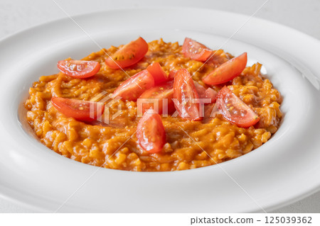 Creamy tomato risotto topped with cherry tomatoes on clean white plate Creamy tomato risotto topped with cherry tomatoes on clean white plate 125039362