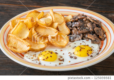 Golden potato dippers, fried eggs, and mushrooms on rustic textured table setting Golden potato dippers, fried eggs, and mushrooms on rustic textured table setting 125039381