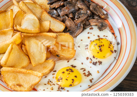Golden potato dippers, fried eggs, and mushrooms on rustic textured table setting Golden potato dippers, fried eggs, and mushrooms on rustic textured table setting 125039383