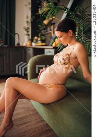 Pregnant young woman relaxing on a green sofa in a cozy indoor setting 125039404