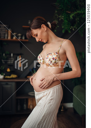 Young pregnant woman gently touching her baby bump in a cozy home setting 125039408