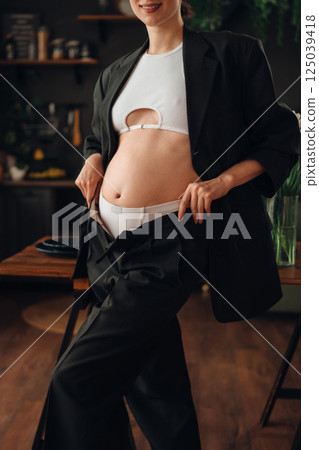 Pregnant young woman posing in stylish outfit at home during daytime Pregnant young woman posing in stylish outfit at home during daytime 125039418