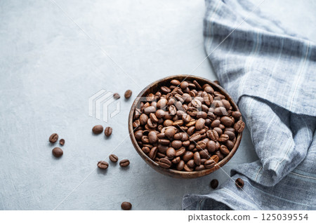 Bowl of roasted coffee beans on table with linen cloth in natural light setup. Bowl of roasted coffee beans on table with linen cloth in natural light setup. 125039554